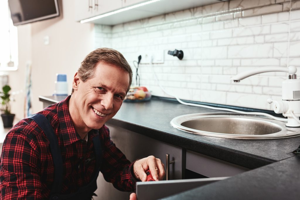 Smiling master. Seniour handyman repairing washbasin with smile
